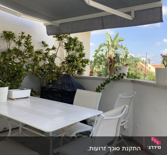 סוכך אפור נפתח מעל מרפסת עם שולחן וכיסאות
